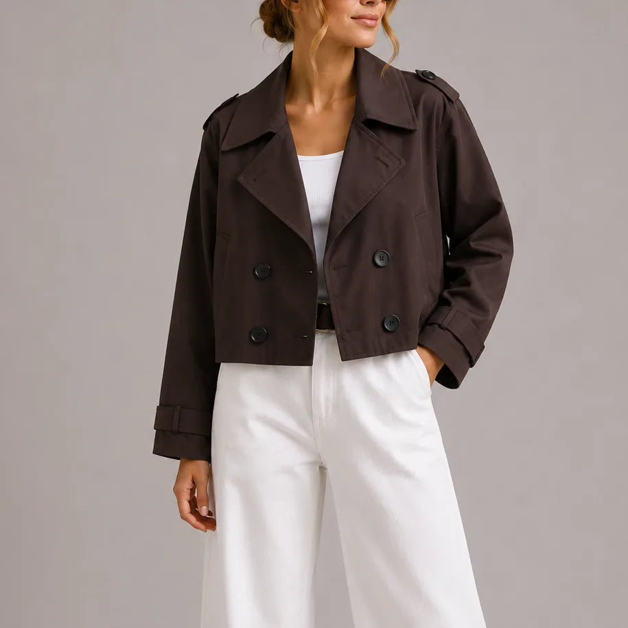 Front view of a woman wearing a dark brown cropped double-breasted trench jacket with wide lapels over a white top