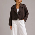 Front view of a woman wearing a dark brown cropped double-breasted trench jacket with wide lapels over a white top
