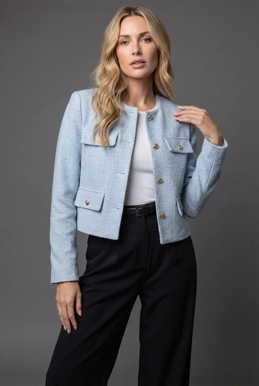 Woman wearing a collarless light blue tweed cropped jacket open over a white top and black tailored trousers
