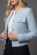 Close-up of the light blue tweed fabric texture with gold buttons and flap pocket detail on the chest