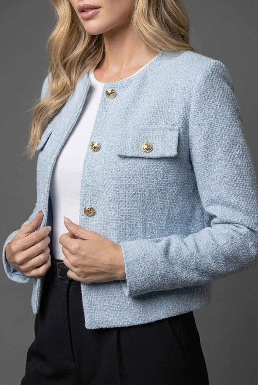 Close-up of the light blue tweed fabric texture with gold buttons and flap pocket detail on the chest