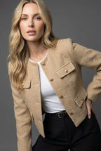 Close-up of a camel beige tweed cropped jacket with gold buttons and two flap pockets on the hip
