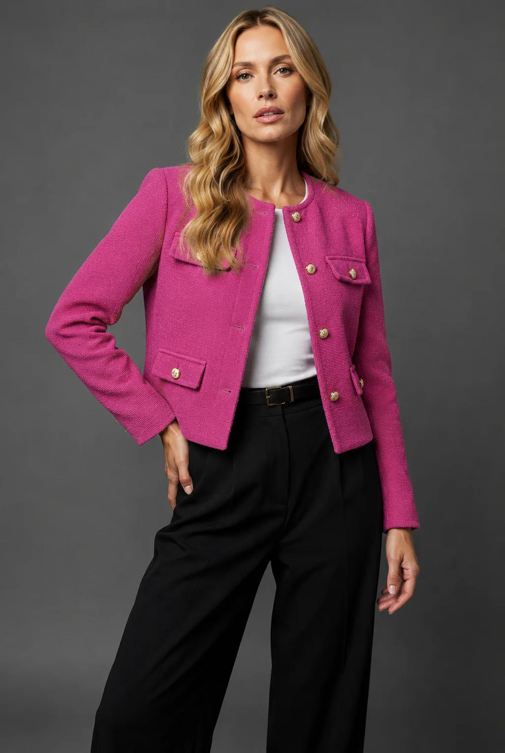 Hot pink tweed cropped jacket with gold buttons and flap pockets worn with high-waisted black trousers