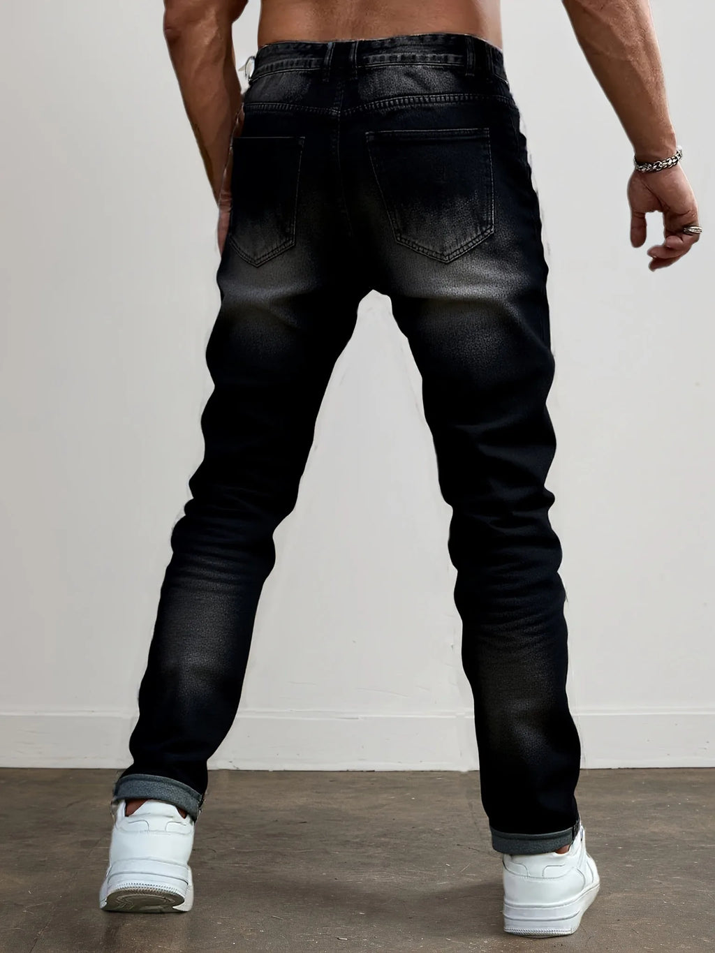 Back view of a model wearing dark grey ripped jeans showing the fit through the leg and rolled hem