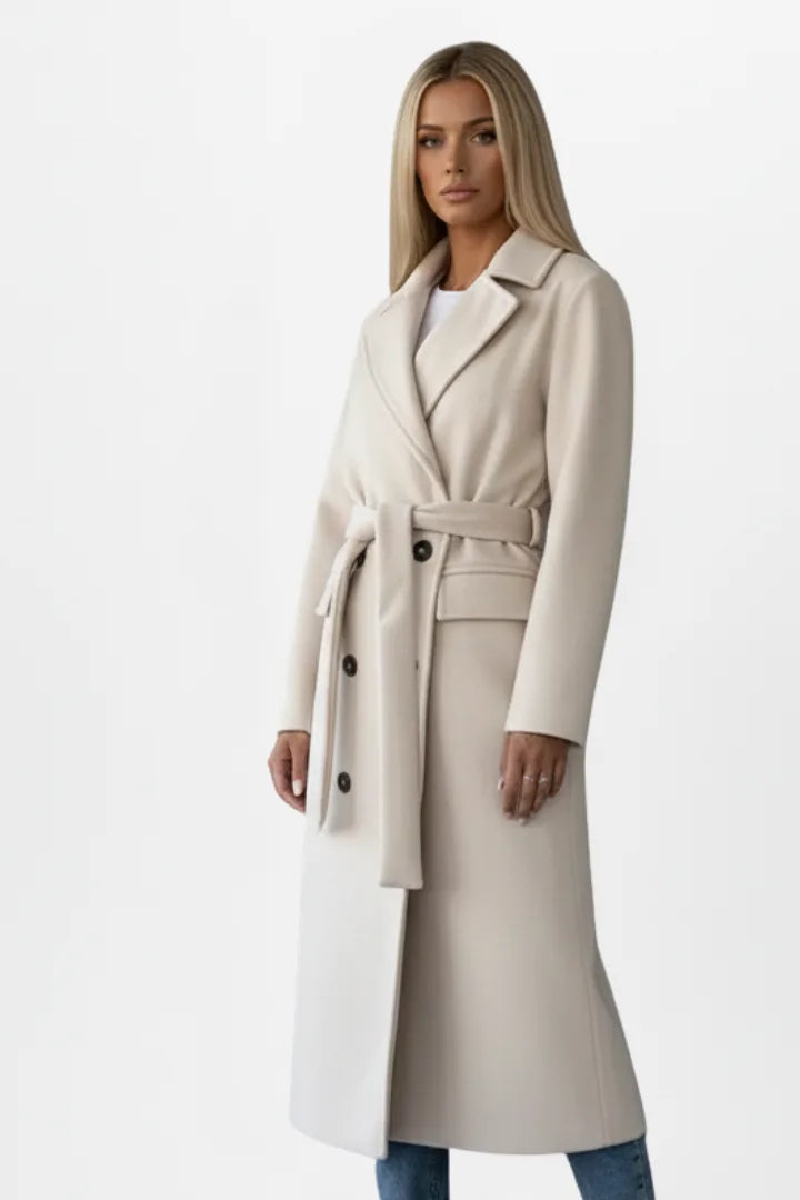 Side angle of a woman in a beige belted coat, showing the flared hem and tailored sleeve