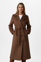 Front view of a woman wearing a mid-brown belted coat with hands in the welt pockets