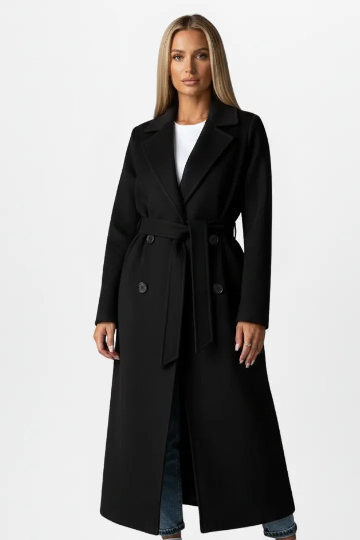 Front view of a woman wearing a black double-breasted longline coat with tie belt over blue jeans
