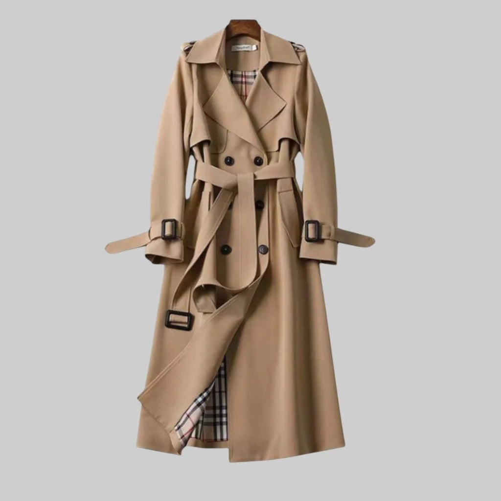 Beige double-breasted trench coat on a wooden hanger, belted waist, checked lining visible at the hem