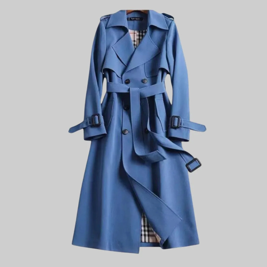 Blue double-breasted trench coat with buckled cuff straps and open belt loops draping down the front