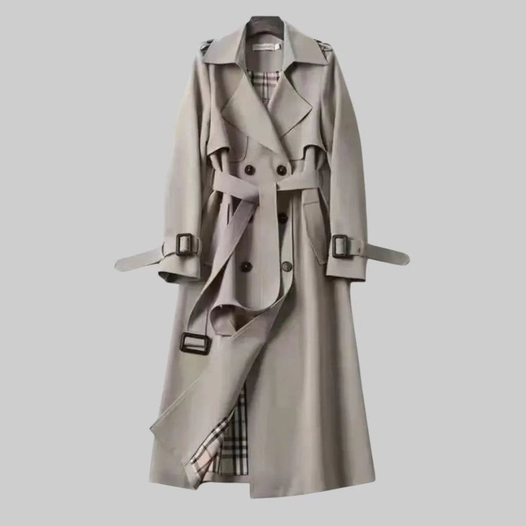 Grey trench coat shown fully buttoned with tie belt and buckled cuffs, midi length on hanger