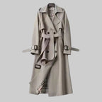 Grey trench coat shown fully buttoned with tie belt and buckled cuffs, midi length on hanger