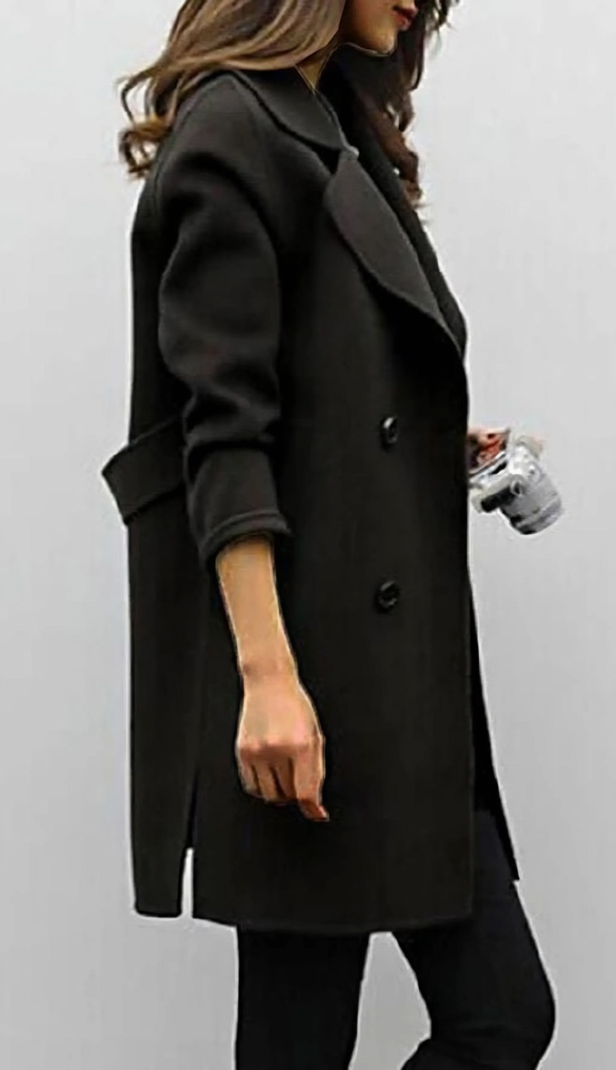 Side profile of black double-breasted coat showing wide lapel, cuffed sleeve and knee-skimming hem