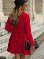 Back view of a red trench coat showing the tie belt knotted at the waist and A-line hem