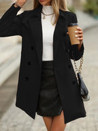Close-up of a black double-breasted trench coat worn open over a white ribbed jumper, holding a coffee cup