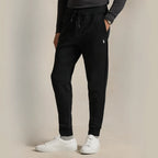 Side view of a man wearing black double-knit joggers with white trainers, hand in pocket