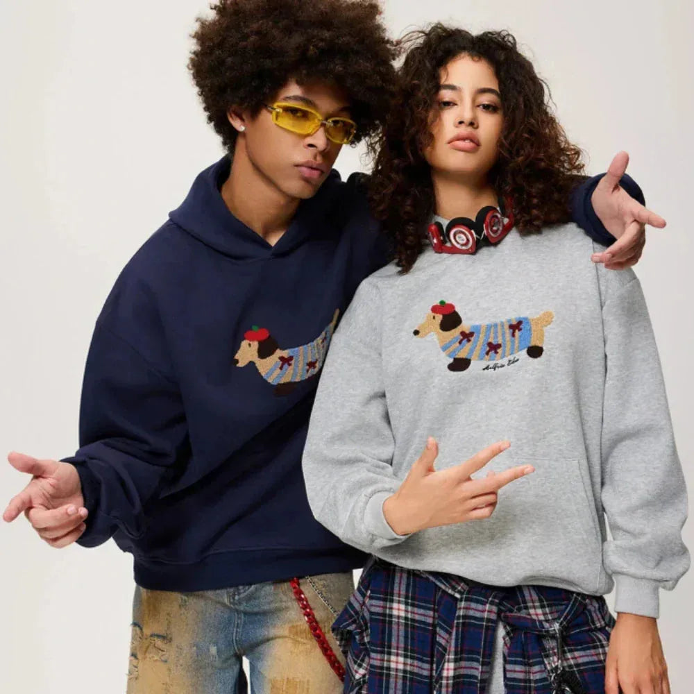 Two models wearing matching hoodies, one navy and one grey, both with the dachshund dog graphic
