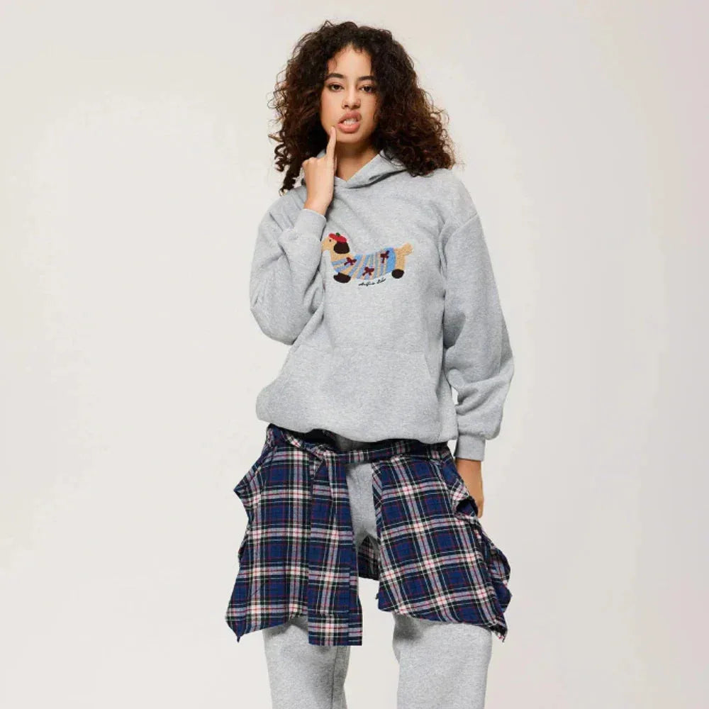 Woman styling a grey hoodie with tartan check trousers, close up of the embroidered dog patch