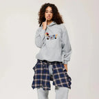 Woman styling a grey hoodie with tartan check trousers, close up of the embroidered dog patch