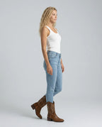 Side view of woman walking in light denim jeans paired with brown embroidered pull-on cowboy boots
