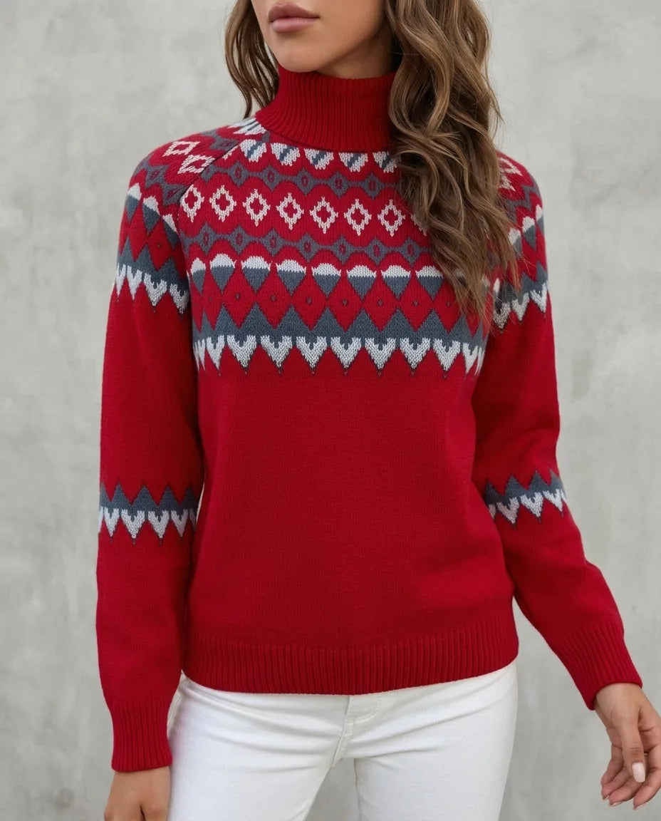 Close-up front view of a red Fair Isle patterned polo neck jumper with grey and white knit detailing, worn with white trousers.