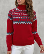 Close-up front view of a red Fair Isle patterned polo neck jumper with grey and white knit detailing, worn with white trousers.