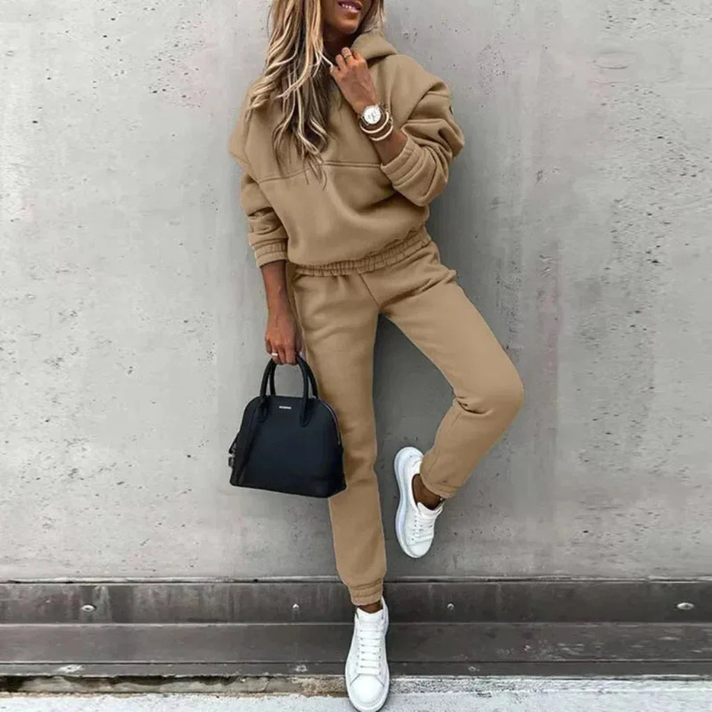 Camel-toned fleece hoodie and jogger tracksuit worn with white trainers, shown against a concrete wall