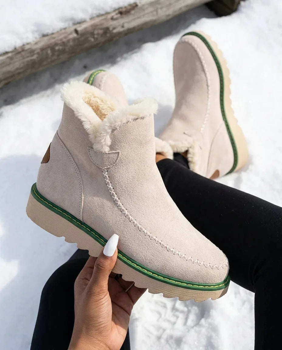 Beige suede platform ankle boot with cream faux fur trim, held by hand against a snowy log backdrop