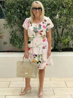 Front view of the cream floral layered midi dress with round neckline, paired with pearl necklace and tote bag