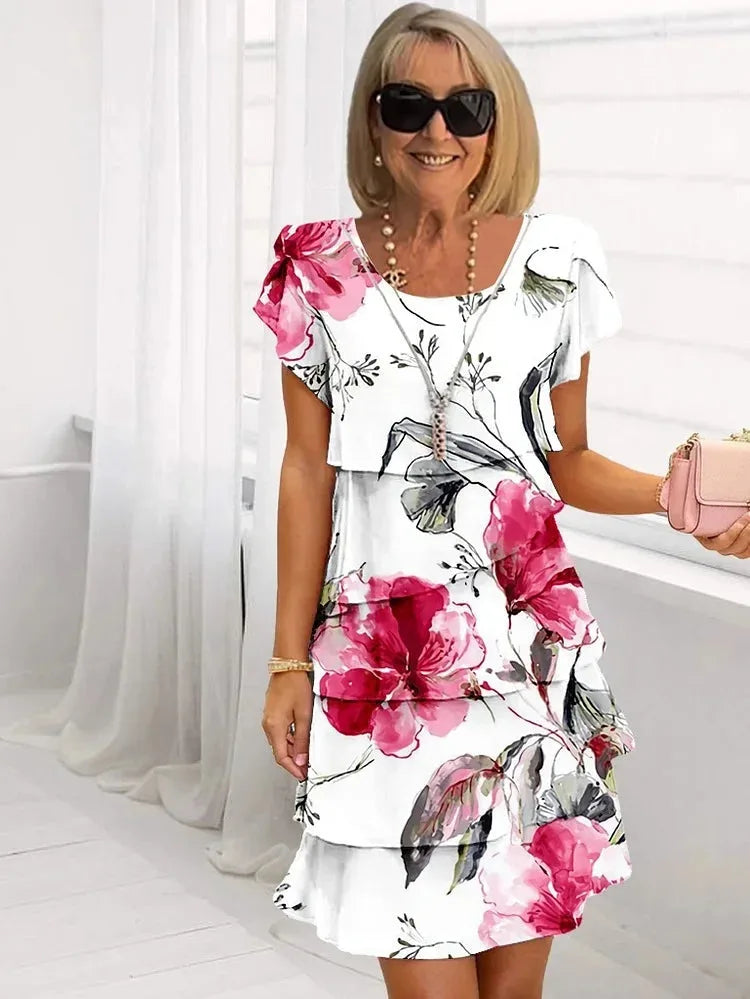 White tiered midi dress with pink and green floral print, short flutter sleeves, worn with a pink clutch