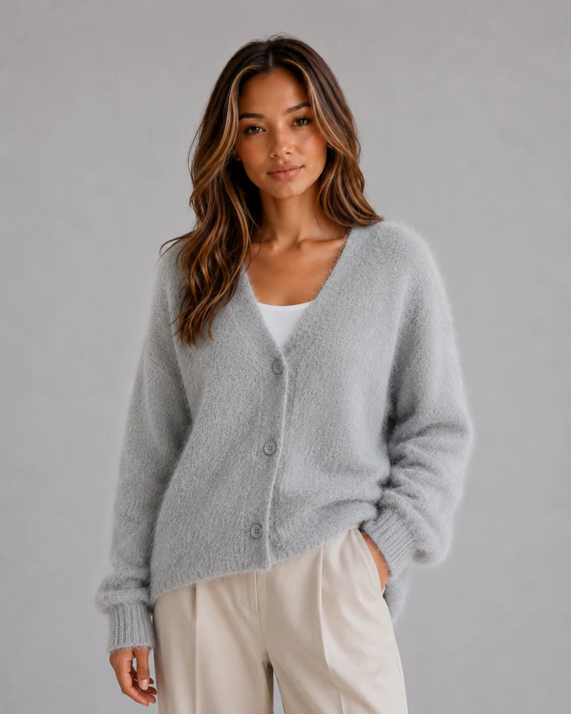 Woman wearing the fluffy knit cardigan in light grey, paired with cream tailored trousers