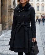 Black double-breasted skater coat with black faux fur collar, tie belt and tiered peplum hem, paired with a handbag