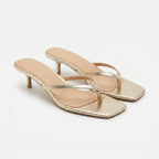 Pair of gold thong-strap kitten heel sandals with square toe and slim heel, shown from a front angle on a white background