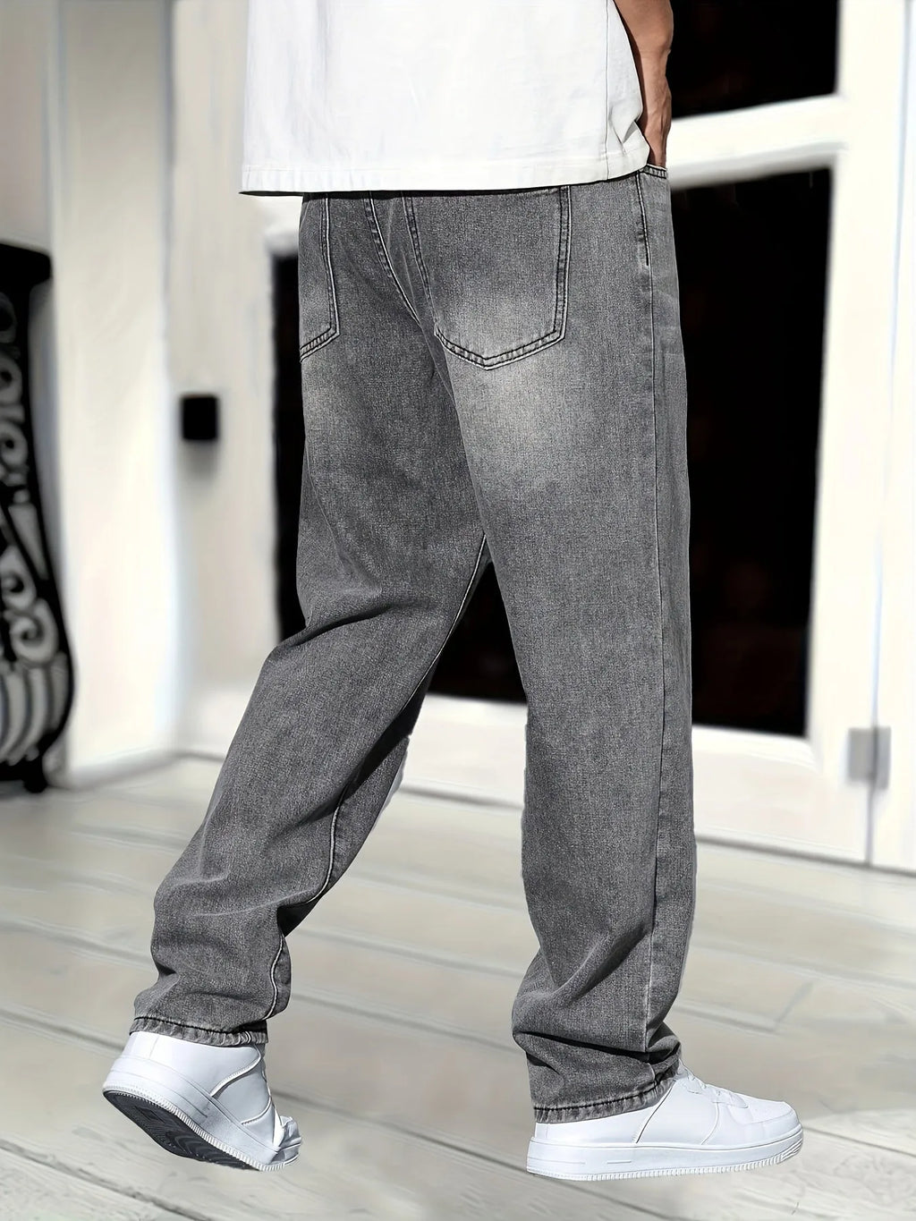 Rear view of grey washed denim jeans showing back pockets, straight leg cut and white trainers