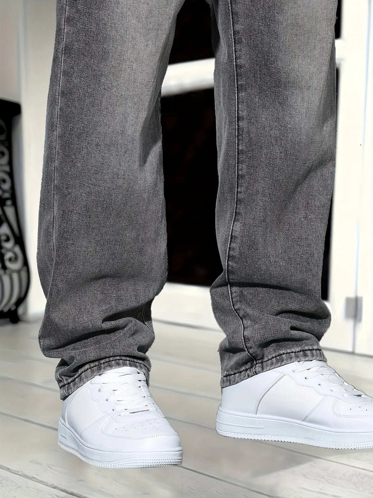 Close-up of lower leg hems showing washed grey denim texture and fit over white trainers