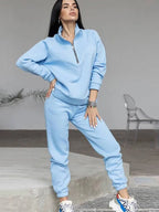 Light blue half-zip tracksuit top with V-seam detail paired with tapered joggers, model posing on a concrete step.