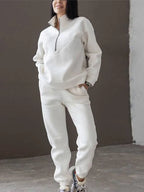 Cream white half-zip fleece jumper and matching joggers shown on a model standing against a warm brown backdrop.
