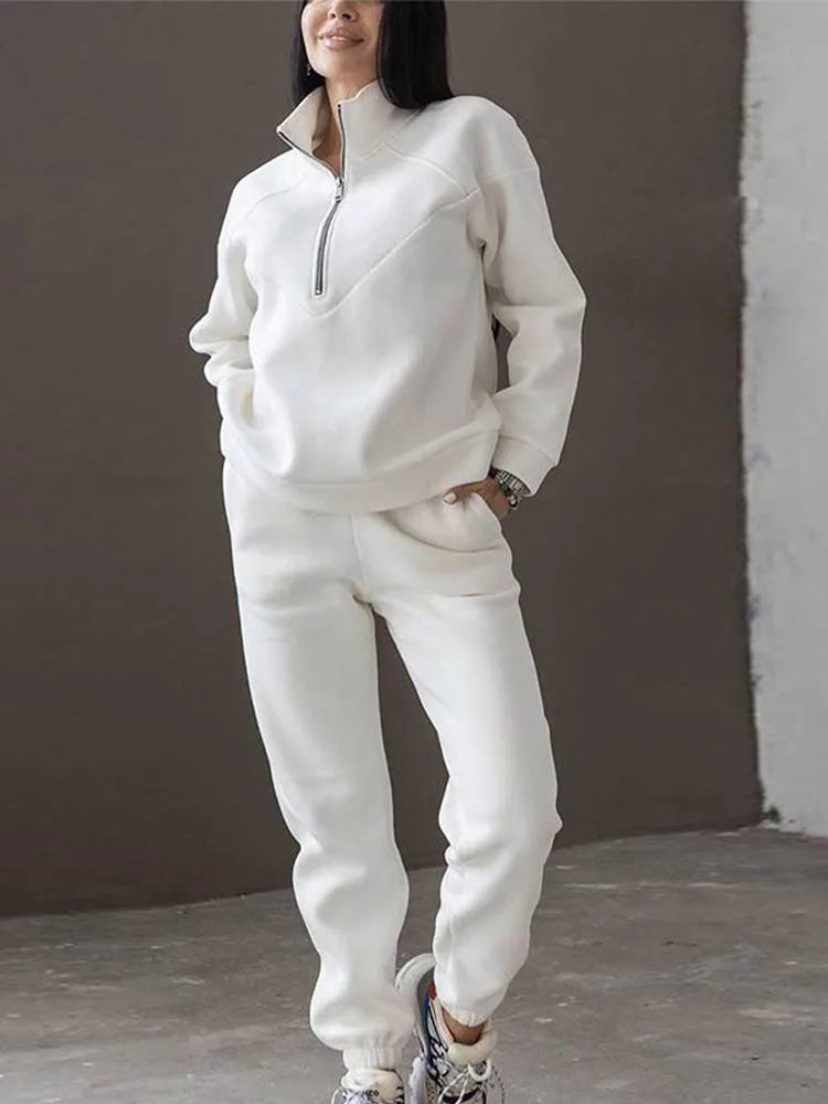 Cream white half-zip fleece jumper and matching joggers shown on a model standing against a warm brown backdrop.