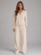 Front view of a woman wearing a cream half zip lounge jumper and matching wide leg trousers with white trainers