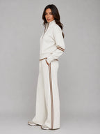 Side profile of woman in cream lounge set with hands in trouser pockets, showing relaxed wide leg fit