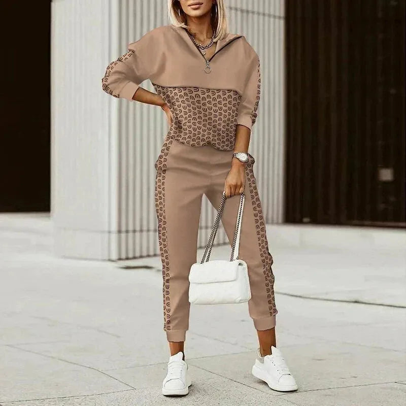 Woman wearing a beige half-zip tracksuit with contrast monogram-print panel across the top and side-striped joggers