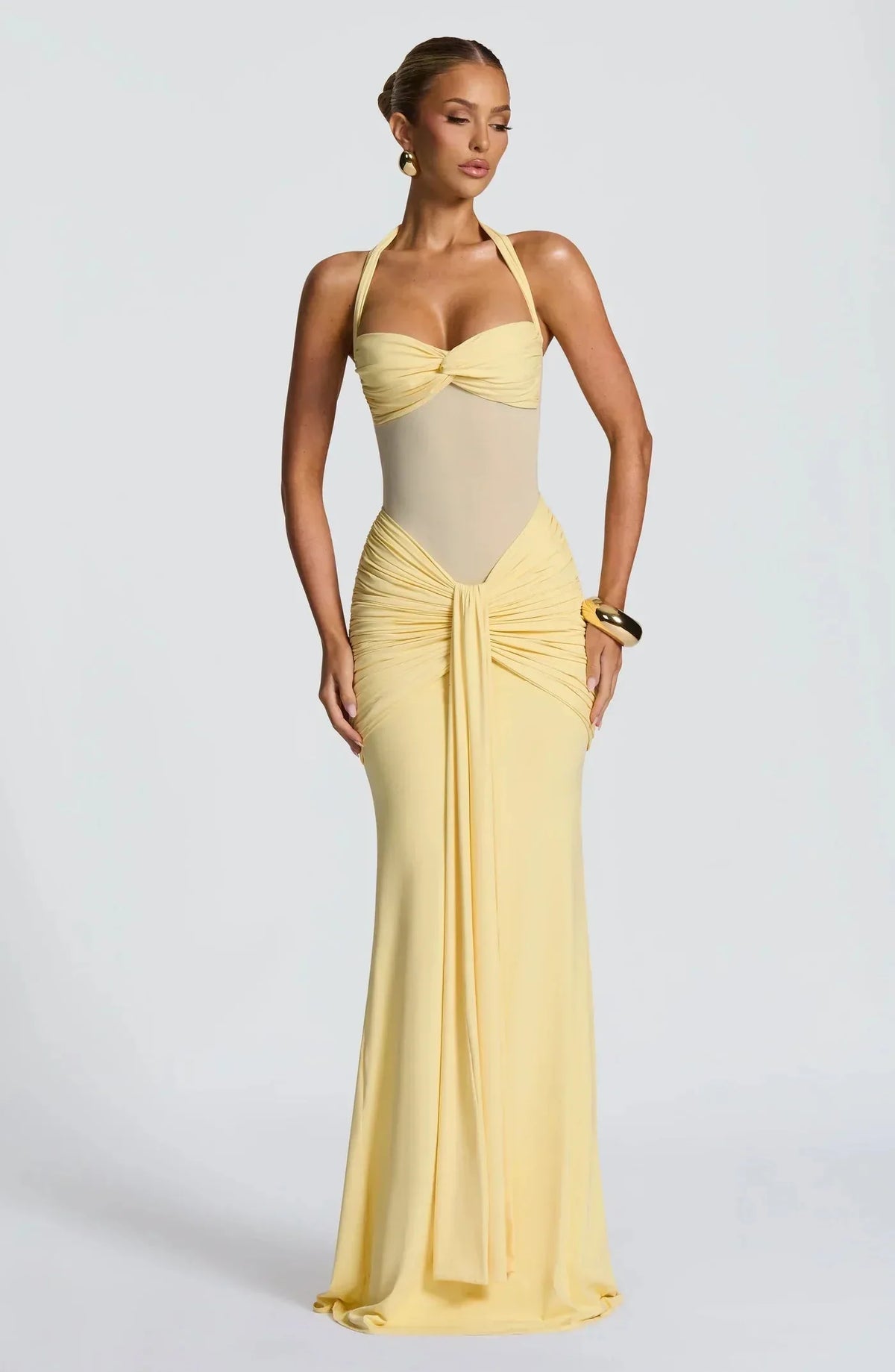 Front view of a pale yellow halter-neck evening gown with sheer mesh waist panel and draped ruched skirt