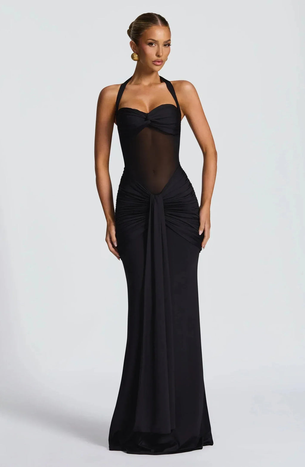 Front view of a black halter-neck evening gown with sheer mesh bodice and draped ruched skirt falling to the floor