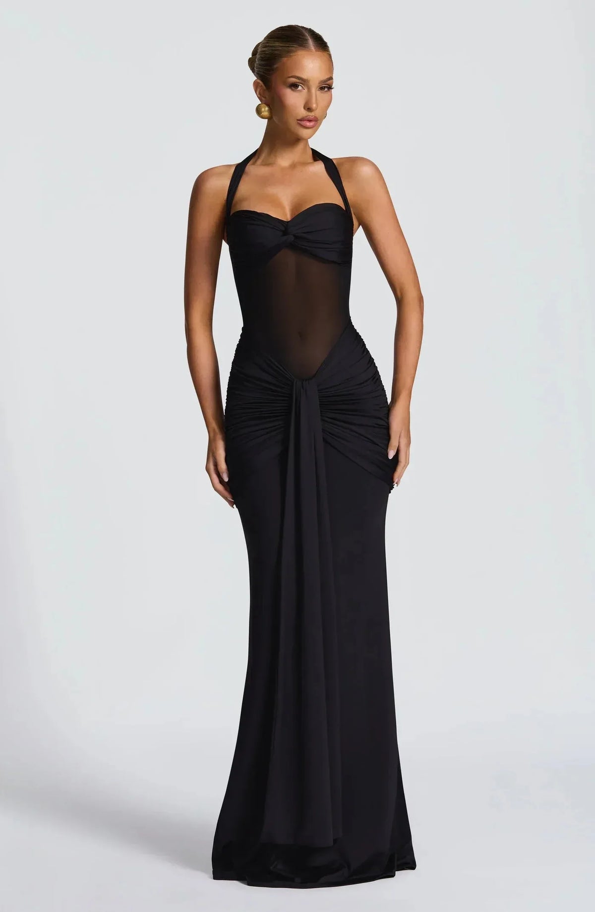 Front view of a black halter-neck evening gown with sheer mesh bodice and draped ruched skirt falling to the floor