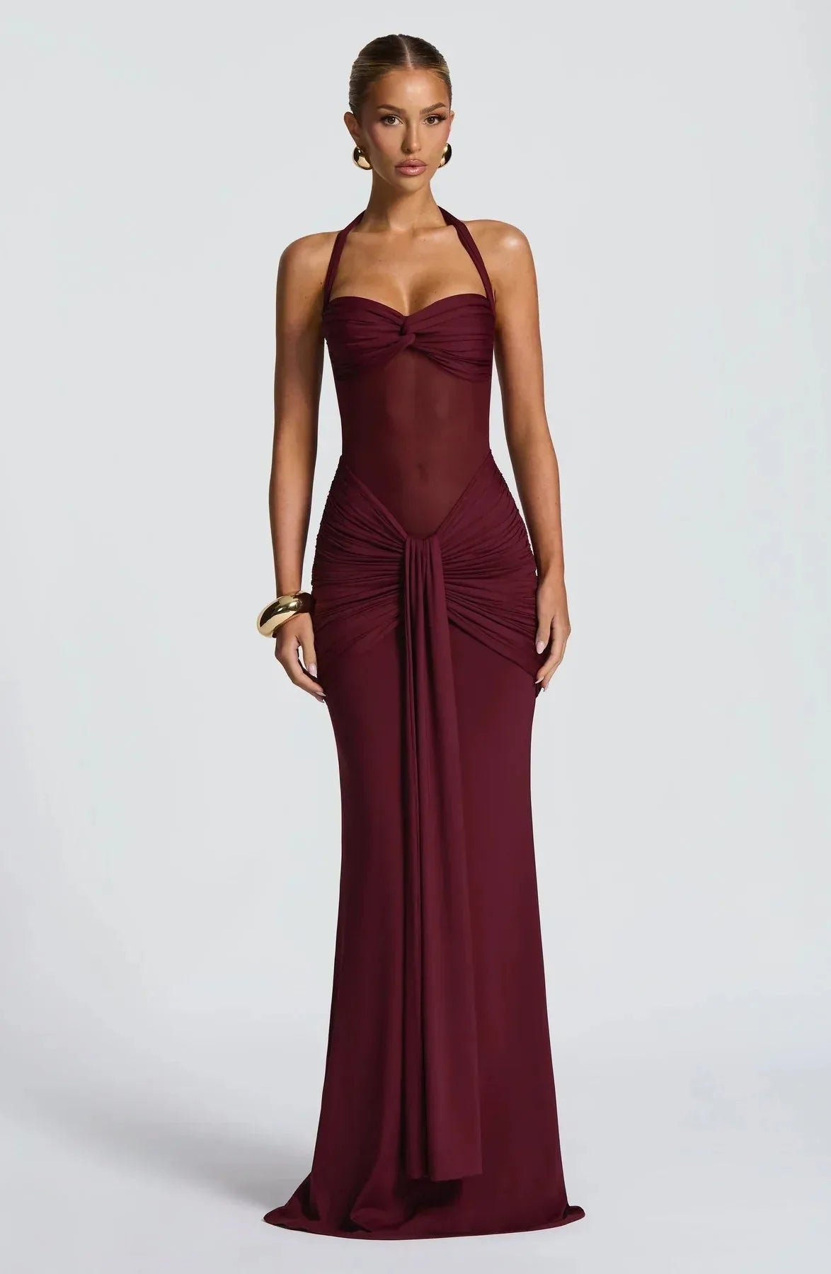 Front view of a burgundy halter-neck maxi dress with sheer mesh waist and draped ruched skirt