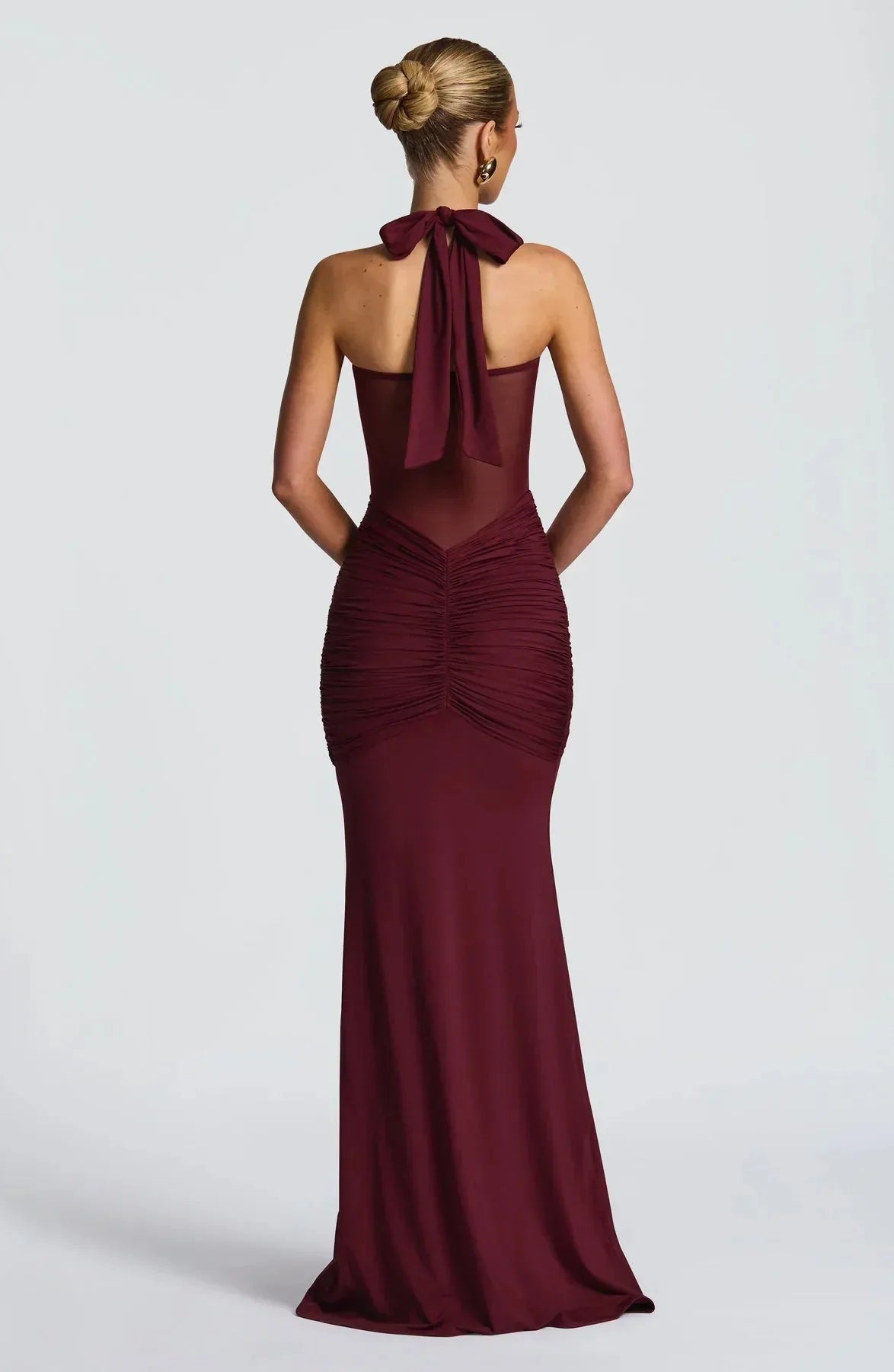 Model wearing the burgundy halter evening dress paired with gold hoop earrings and a statement bangle