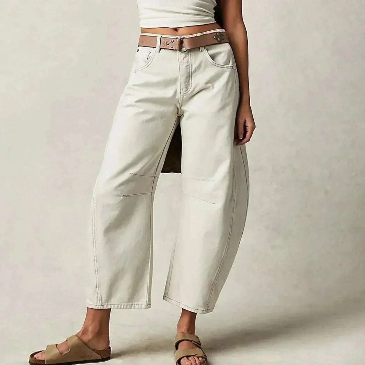 Off-white barrel-leg jeans styled with a brown leather belt and neutral slide sandals