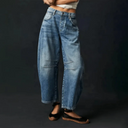 Light-wash blue denim barrel jeans paired with black espadrille flats against a dark backdrop