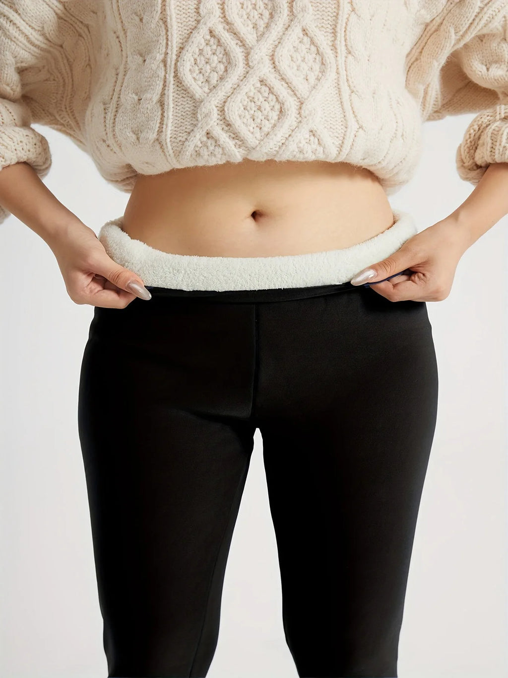 Front close-up of black leggings waistband peeled back showing plush cream fleece lining against bare skin