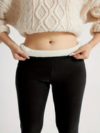Front close-up of black leggings waistband peeled back showing plush cream fleece lining against bare skin