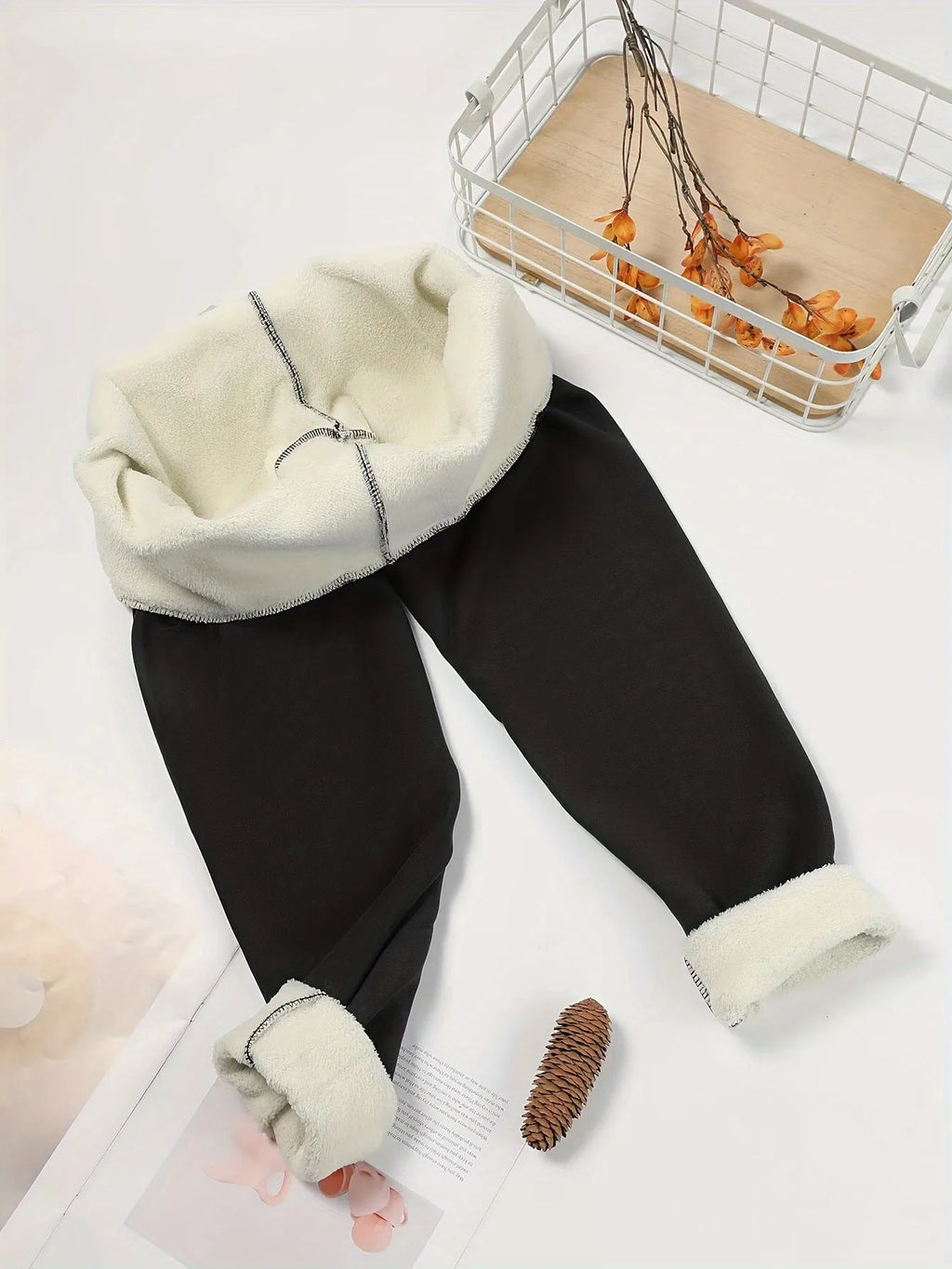 Flat lay of black fleece-lined leggings with cuffs turned inside out to display cream sherpa fleece lining